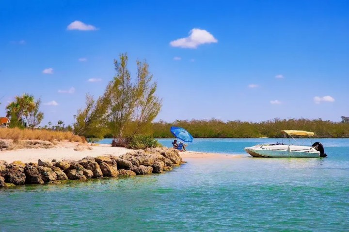 Small beach area with a boat, people, and umbrella under clear blue sky.