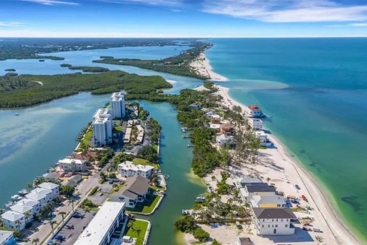 Aerial view of beach, buildings, and ocean under blue sky.
