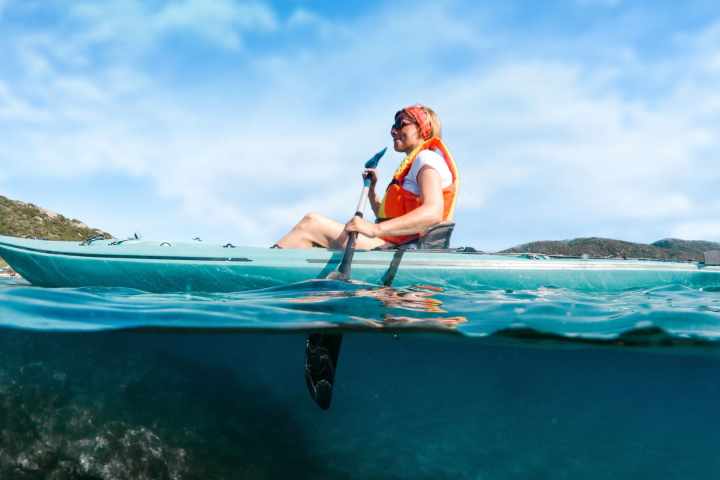 Person in a kayak on clear water with sky and hills in background.