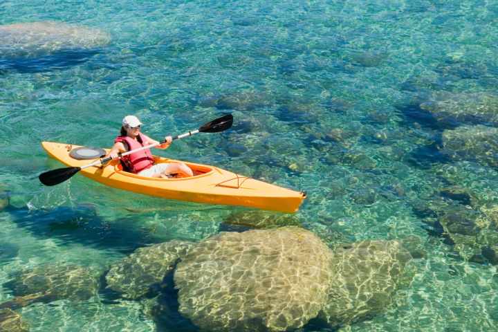 Person kayaking on clear blue water with visible rocks below.
