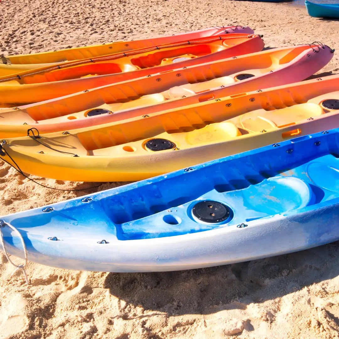 Five colorful kayaks on a sandy beach, lined up diagonally.