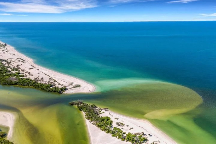 Aerial view of a coastal landscape with a sandbar and green-blue sea.