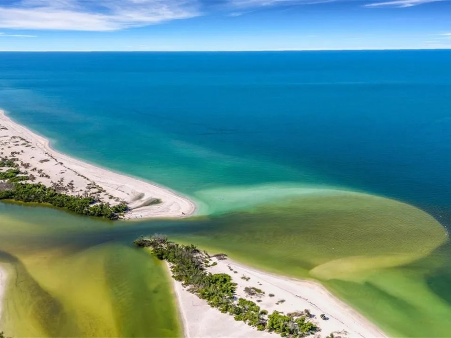 Aerial view of a coastal landscape with a sandbar and green-blue sea.