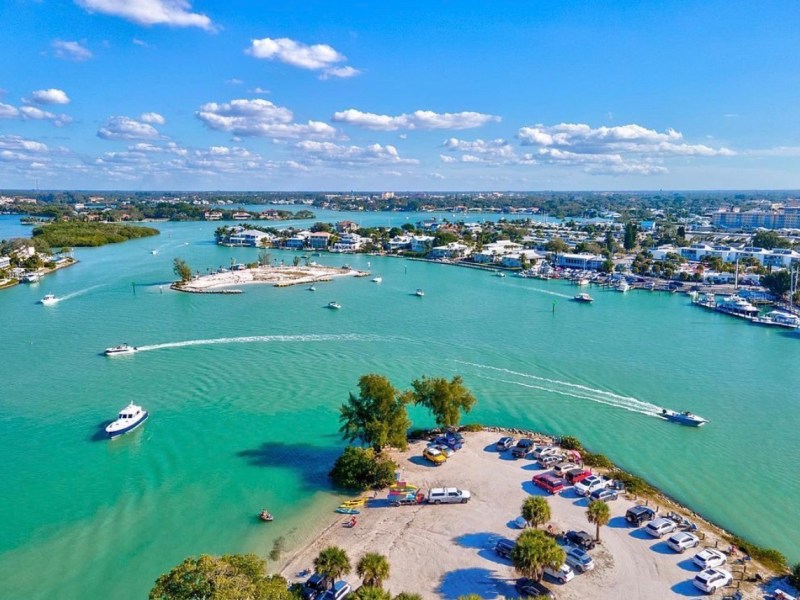 Aerial view of turquoise waters, small boats, and a waterfront town under a clear blue sky.