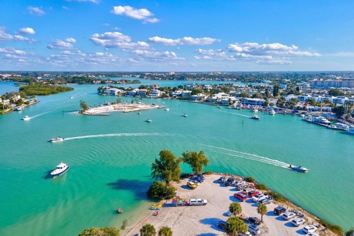 Aerial view of a vibrant turquoise bay with boats and a small island under a clear blue sky.