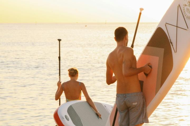 Two people with paddleboards and paddles at sunset by the sea.