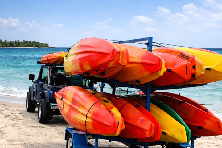 Jeep with kayak trailer carrying colorful kayaks on a sandy beach.