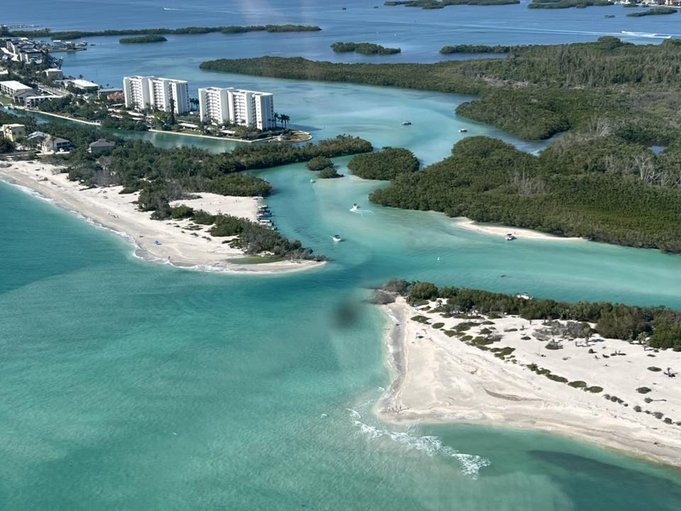 Aerial view of beach, turquoise water, and nearby buildings.