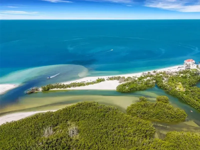 Aerial view of a coastal area with sandy beach, turquoise water, and green vegetation.